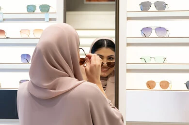 Looking in the mirror with an expression of happiness and pleasure, enjoying shopping in the Emirates, modern women's accessories, choosing suitable sunglasses, an Emirati woman trying on glasses before buying, a close-up from the back of a veiled Saudi Arabian Gulf young woman wearing an abaya trying on glasses