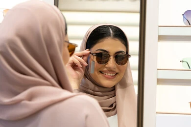 The joy of shopping in the Emirates, modern women's accessories, choosing suitable sunglasses, taking care of one's appearance, an Emirati woman trying on glasses before buying, a close-up photo from the back of a veiled Saudi Arabian Gulf young woman wearing an abaya trying on her glasses and looking at them in the mirror