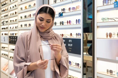 Buying stylish, modern women's accessories, keeping up with the latest fashion and beauty trends, enjoying shopping in the UAE malls, a Saudi woman examining colored glasses, a veiled young Emirati Gulf Arab woman wearing an abaya choosing sunglasses that suit her facial features