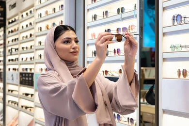 Following the latest fashion and beauty trends, the joy of shopping in the Emirates malls, elegant, modern women's accessories, a close-up of a Saudi woman examining colored glasses, a veiled young Arab Gulf Emirati woman wearing an abaya choosing sunglasses that suit her facial features
