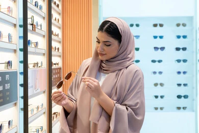 Caring about one's appearance, the latest women's accessories, enjoying shopping in the UAE malls, keeping up with the latest fashion and beauty trends, a veiled young Emirati Gulf Arab woman wearing an abaya choosing sunglasses that suit her facial features, a Saudi woman examining glasses