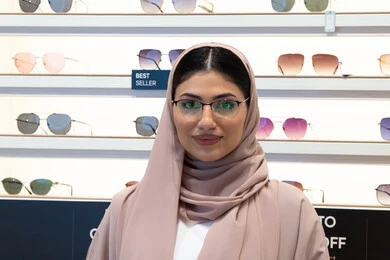 تعابير الثقة بالنفس، مفهوم ضعف النظر،الشراء من المحلات الإماراتية، اختيار نظارة ملائمة لملامح الوجه،  اقتناء نظارات طبية جديدة، صورة مقربة لشابة عربية خليجية سعودية محجبة ترتدي عباءة تنظر إلى الكاميرا بإيماءات السعادة، امرأة إماراتية تقوم بمعاينة النظارات