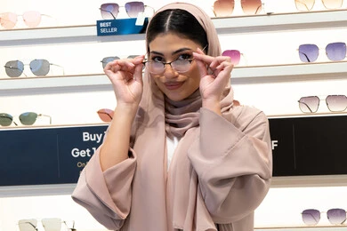 Self-confidence gestures, the concept of weak eyesight, shopping from Emirati stores, choosing glasses that fit facial features, acquiring new eyeglasses, a close-up of a veiled Saudi Arabian Gulf young woman wearing an abaya looking at the camera with happy gestures, an Emirati woman examining eyeglasses