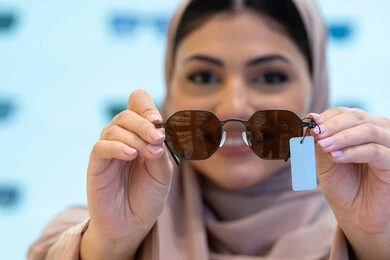 اختيار نظارة شمسية ملائمة لملامح الوجه، اكسسوارات نسائية عصرية أنيقة، النظر إلى الكاميرا بإيماءات السرور، الاستمتاع بالتسوق في الإمارات، امرأة اماراتية تقوم بتجربة النظارات قبل الشراء، صورة مقربة لشابة عربية خليجية سعودية محجبة ترتدي عباءة تقوم بقياس نظاره