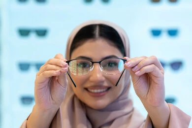 The joy of shopping in the Emirates Malls, correcting and improving vision, the concept of weak vision, looking at the camera with happy gestures, buying new eyeglasses, a close-up of a young Saudi Arabian Gulf woman wearing an abaya choosing eyeglasses that suit her facial features, an Emirati woman examining eyeglasses