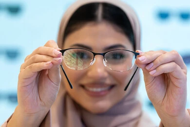 Correcting and improving vision, the pleasure of shopping in the Emirates malls, the concept of weak vision, looking at the camera with happy gestures, buying new eyeglasses, a close-up of a young Saudi Arabian Gulf woman wearing an abaya choosing eyeglasses that suit her facial features, an Emirati woman examining eyeglasses