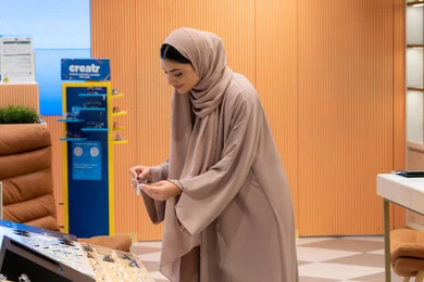 مفهوم الاهتمام بالمظهر الخارجي، مواسم التخفيضات في الإمارات، مواكبة آخر صيحات الموضة والجمال، شابة عربية خليجية اماراتية محجبة ترتدي عباءة تقوم باختيار نظارة شمسية ملائمة لملامح الوجه، امرأة سعودية تقوم بمعاينة النظارات