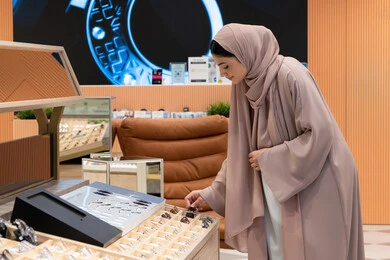 الاهتمام بالمظهر الخارجي، مواسم التخفيضات في الإمارات، مواكبة آخر صيحات الموضة والجمال، شابة عربية خليجية اماراتية محجبة ترتدي عباءة تقوم باختيار نظارة شمسية ملائمة لملامح الوجه، امرأة سعودية تقوم بمعاينة النظارات