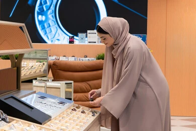 مواكبة آخر صيحات الموضة والجمال، الاهتمام بالمظهر الخارجي، أحدث الاكسسوارات النسائية، المتعة بالتسوق في مولات الإمارات، شابة عربية خليجية اماراتية محجبة ترتدي عباءة تقوم باختيار نظارة شمسية ملائمة لملامح الوجه، امرأة سعودية تقوم بمعاينة النظارات