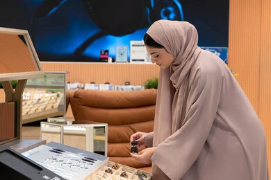 حماية العينين من أشعة الشمس، مواكبة آخر صيحات الموضة والجمال، الاهتمام بالمظهر الخارجي، المتعة بالتسوق في مولات الإمارات، شابة عربية خليجية اماراتية محجبة ترتدي عباءة تقوم باختيار نظارة شمسية ملائمة لملامح الوجه، امرأة سعودية تقوم بمعاينة النظارات
