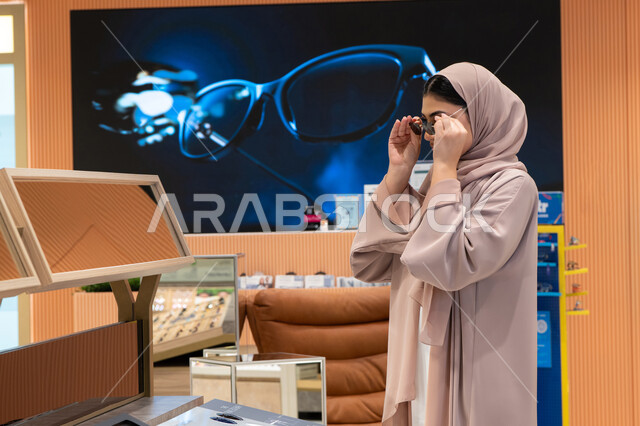 الاهتمام بالمظهر الخارجي، اكسسوارات نسائية عصرية، التأثير الإيجابي للتسوق على المرأة، تجربة النظارات الشمسيه قبل الشراء، شابة اماراتية تقوم باختيار نظارة شمسيه مناسبة، سيدة عربية خليجية سعودية محجبة ترتدي عباءة تقوم بقياس نظاره
