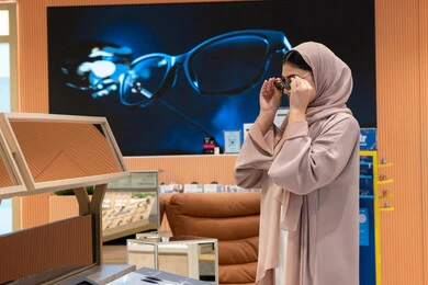الاهتمام بالمظهر الخارجي، اكسسوارات نسائية عصرية، التأثير الإيجابي للتسوق على المرأة، تجربة النظارات الشمسيه قبل الشراء، شابة اماراتية تقوم باختيار نظارة شمسيه مناسبة، سيدة عربية خليجية سعودية محجبة ترتدي عباءة تقوم بقياس نظاره