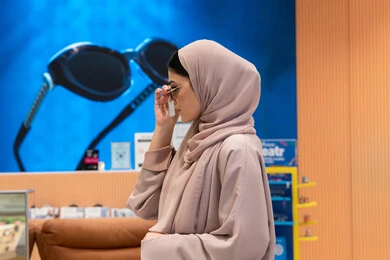 اكسسوارات نسائية عصرية، الاهتمام بالمظهر الخارجي، التأثير الإيجابي للتسوق على المرأة، تجربة النظارات الشمسيه قبل الشراء، شابة اماراتية تقوم باختيار نظارة شمسيه مناسبة، سيدة عربية خليجية سعودية محجبة ترتدي عباءة تقوم بقياس نظاره