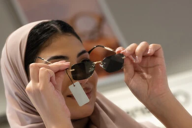 Shopping in UAE malls and stores, trying on sunglasses before buying, international brands and types, a Saudi woman choosing suitable sunglasses, a close-up of a smiling veiled Emirati Gulf Arab woman wearing an abaya trying on her glasses with gestures of happiness and pleasure