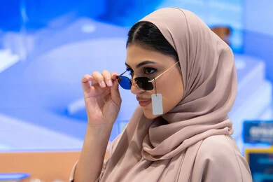 Enjoy shopping and buying, international types and brands, wearing sunglasses before buying, a Saudi woman choosing suitable sunglasses, a close-up side view of a veiled Emirati Gulf Arab woman wearing an abaya trying on her glasses with gestures of self-confidence