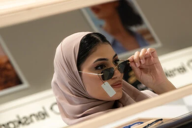 انواع وماركات عالميه، ارتداء النظارات الشمسيه قبل الشراء، متعة التسوق والشراء، سيدة سعودية تقوم باختيار نظارة شمسيه مناسبة، صورة مقربة لامرأة عربية خليجية إماراتية محجبة ترتدي عباءة تقوم بقياس نظاره بإيماءات الثقة بالنفس