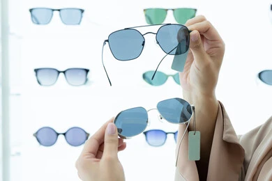 الحيرة في اختيار نظارة مناسبة، معرض نظارات شمسية، الاستفادة من العروض والتخفيضات، مواكبة آخر صيحات الموضة والجمال، صورة مقربة لأيدي شابة عربية خليجية اماراتية  تقوم باختيار نظارة شمسية ملائمة لملامح الوجه، امرأة سعودية تقوم بمعاينة النظارات