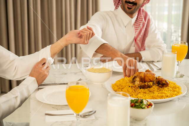 حسن إكرام واستقبال الضيف، تقديم الكبسه السعوديه على المائده، إيماءات السعادة و السرور بقضاء وقت ممتع مع الأصدقاء، دعوة العائلة لتناول وجبة شهيه, الاجتماع على طاولة الطعام، صورة مقربة لصديقين عربيين خليجيين سعوديين يرتديان الزي التقليدي يتناولان الغداء