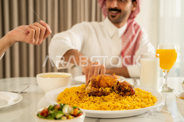 حسن إكرام واستقبال الضيف، تقديم الكبسه السعوديه على المائده، إيماءات السعادة و السرور بقضاء وقت ممتع مع الأصدقاء، دعوة العائلة لتناول وجبة شهيه, الاجتماع على طاولة الطعام، صورة مقربة لصديقين عربيين خليجيين سعوديين يرتديان الزي التقليدي يتناولان الغداء