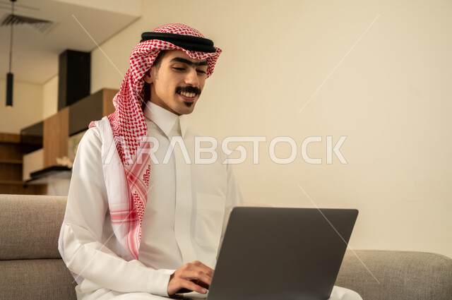 متابعة الأفلام والمسلسلات، تصفح مواقع الانترنت والعمل عن بعد، الاجتهاد وانجاز الاعمال المطلوبة، استخدام التقنية الحديثة، إحتراف وظائف الحاسوب وتكنولوجيا المعلومات، رجل عربي خليجي سعودي يرتدي الزي التقليدي يجلس على الأريكة في غرفة المعيشة ويقوم باستخدام اللابتوب