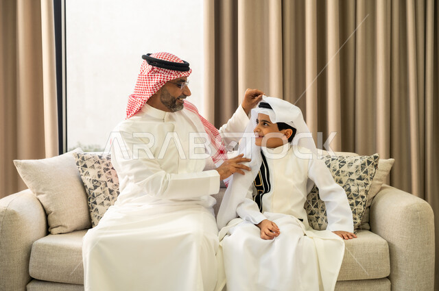 الاهتمام بالأناقة والمظهر الخارجي، الدردشة والمحادثة مع الأحفاد, فتى عربي خليجي سعودي يرتدي الزي التقليدي يجلس مع جده يحتفلون في العيد المبارك,  قضاء اوقات عائلية ممتعة في الاعياد والمناسبات الاسلامية المباركة