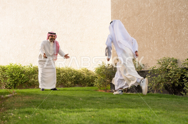 أعياد ومناسبات اسلامية سعيدة, فرحة الأطفال بقدوم العيد, الاستمتاع مع الأبناء في الهواء الطلق, ايماءات تدل على الحماس والسعاده، ولد عربي خليجي سعودي يرتدي الزي التقليدي يركض باتجاه والده و يفتح يديه لاحتضانه، قضاء أوقات عائلية ممتعة في المنتجع السياحي