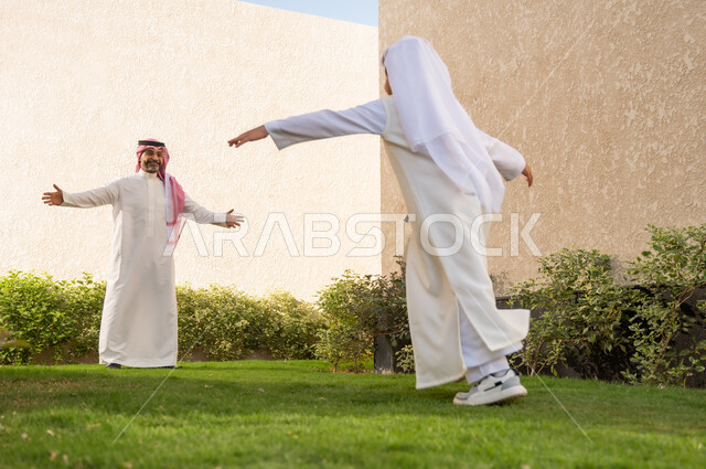 أعياد ومناسبات اسلامية سعيدة, فرحة الأطفال بقدوم العيد, الاستمتاع مع الأبناء في الهواء الطلق, ايماءات تدل على الحماس والسعاده، ولد عربي خليجي سعودي يرتدي الزي التقليدي يركض باتجاه والده و يفتح يديه لاحتضانه، قضاء أوقات عائلية ممتعة في المنتجع السياحي