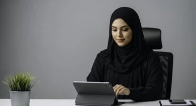 Saudi female office profession and job, managing and completing tasks using a modern and advanced technical device, close-up portrait of a smiling Saudi Arabian Gulf woman wearing hijab and abaya working on a portable tablet, gestures and expressions of pleasure and happiness, gray background