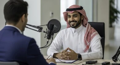 معدات وأجهزة تسجيلات الصوت، اجراء بث صوتي مباشر ( بودكاست ) عبر برامج التواصل الاجتماعي، ايماءات الحماس والتفاعل، تعابير السعادة والسرور، رجل عربي خليجي سعودي يرتدي الثوب والشماغ التقليدي مع رجل بالبدلة الرسمية في مقابلة عمل داخل مقر الشركة