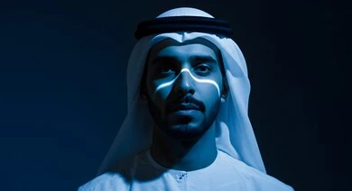 النظر الى الكاميرا بايماءات الجدية والحزم، تعابير الثقة بالنفس، الاهتمام بالمظهر الخارجي, مفهوم الأناقة والرجولة, بورتريه مقرب لرجل عربي خليجي اماراتي يرتدي الكندورة يقف لالتقاط الصور الشخصية للوثائق الرسمية، خلفية داكنة مع اضاءة درامية