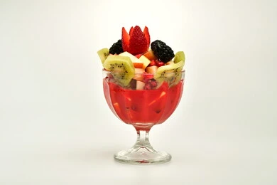Delicious cold desserts, foods and meals full of sugar and high calories, a cup of fruit salad filled with fresh fruits, cream and delicious nuts, white background