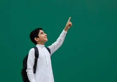 The start of the school year in Saudi schools, the quality of education and learning in the Kingdom, a portrait of a Saudi Arabian Gulf student carrying a school backpack, returning to the classroom with gestures of enthusiasm and joy, a green background