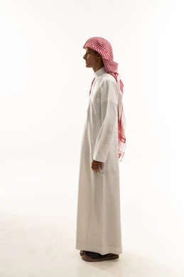 Gestures of handsomeness and masculinity, the concept of attention to external appearance, a side portrait of a young Arab Gulf Saudi boy wearing a thobe and a shemagh, full-body, white background.