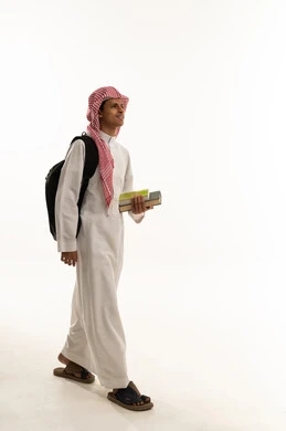 Gestures of walking and going to a specific place, the concept of striving to achieve success, educational scientific curricula, the concept of returning to school, a portrait of an Arab Gulf Saudi student wearing a white thobe and a shemagh, carrying a backpack and school books, looking with gestures of happiness and joy, full-body image, white background.