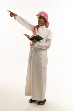Diligence and hard work to achieve success and excellence, the back-to-school season, pointing with the hand to something distant, a portrait of an Arab Gulf Saudi boy wearing traditional attire and a shemagh holding a book in his hand, looking with gestures of happiness and joy, full-body, white background.