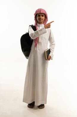 موسم العودة إلى المدارس، الإشارة باليد إلى شيء ما ، الجد والاجتهاد للوصول إلى النجاح والتفوق، بورتريه لطالب عربي خليجي سعودي يرتدي الثوب التقليدي و الشماغ يحمل حقيبة الظهر و الكتب المدرسية ينظر بإيماءات السعادة و السرور، الجسم بالطول الكامل، خلفية بيضاء