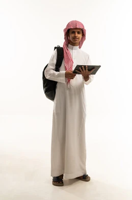 Spending enjoyable time online, using modern technological devices, the concept of education and completing tasks remotely, a portrait of an Arab Saudi Gulf student wearing traditional thobe and shemagh with a backpack using a tablet, playing on the tablet, full-body shot, white background.
