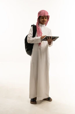 استخدام الأجهزة التقنية الحديثة، مفهوم التعليم وإنجاز المهام عن بعد، بورتريه لطالب عربي سعودي خليجي يرتدي الثوب التقليدي و الشماغ و حقيبة الظهر يقوم باستخدام التابلت، قضاء وقت ممتع على الإنترنت، اللعب على الجهاز اللوحي، الجسم بالطول الكامل، خلفية بيضاء