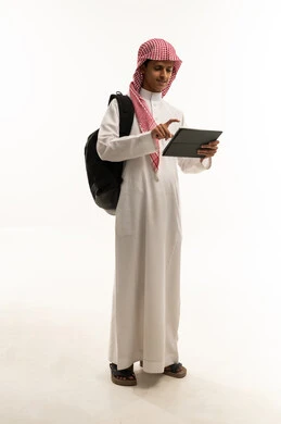 مفهوم التعليم وإنجاز المهام عن بعد، استخدام الأجهزة التقنية الحديثة، بورتريه لطالب عربي سعودي خليجي يرتدي الثوب التقليدي و الشماغ و حقيبة الظهر يقوم باستخدام التابلت، قضاء وقت ممتع على الإنترنت، اللعب على الجهاز اللوحي، الجسم بالطول الكامل، خلفية بيضاء
