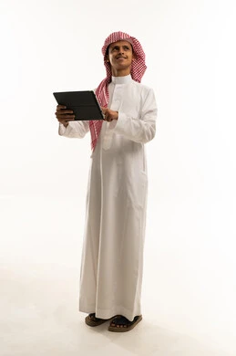 Looking at something, searching for useful and important information, a portrait of an Arab Gulf Saudi boy wearing traditional attire and a shemagh holding a tablet in his hand, merging technology with learning, attending online educational courses, full-body image, white background.