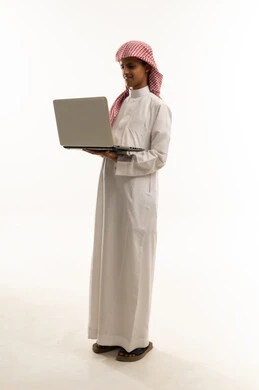 The concept of distance education, gestures of engagement and focus, a portrait of a Saudi Arabian Gulf Arab boy wearing traditional attire and a ghutrah, using a laptop for research, reading, and browsing electronic applications, full-body, white background. The concept of distance education, gestures of engagement and focus, a portrait of a Saudi Arabian Gulf Arab boy wearing traditional attire and a ghutrah, using a laptop for research, reading, and browsing electronic applications, full-body, white background.