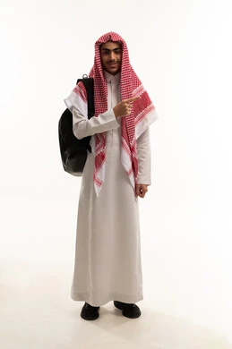 الإشارة باليد إلى شيء ما بعيد، موسم العودة إلى المدارس، الجد والاجتهاد للوصول إلى النجاح والتفوق، بورتريه لطالب عربي خليجي سعودي يرتدي الثوب التقليدي و الشماغ يحمل حقيبة الظهر  ينظر بإيماءات السعادة و السرور، الجسم بالطول الكامل، خلفية بيضاء