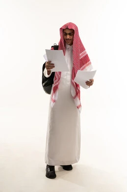 التعليم الثانوي في سلطنه المملكة العربية، الاستعداد للعام الدراسي الجديد , بورتريه لطالب ثانوي عربي خليجي عماني يرتدي الثوب الابيض و الشماغ يحمل حقيبة على ظهره ويمسك بيديه ورق دراسي , الجسم بالطول الكامل, خلفية بيضاء