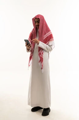 الاطمئنان على الاهل والاصدقاء ، تصفح مواقع التواصل الاجتماعي , بورترية لصبي عربي خليجي سعودي يرتدي الثوب التقليدي و الشماغ يقوم باستخدام الهاتف المحمول, دمج التقنيات الحديثة فى الحياة اليومية, ايماءات السعادة و السرور، الجسم بالطول الكامل، خلفية بيضاء