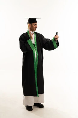 Communication with family and friends, raising the hand with gestures of peace and welcome, the concept of diligence and excellence, celebrating the completion of university studies, using modern technology, a portrait of a young Arab Gulf Saudi graduate wearing a cloak and graduation cap making a call on a mobile phone, full-body, white background.