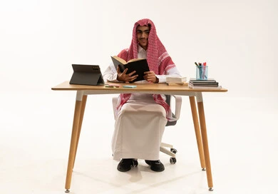مراجعة الدروس اليومية، التعليم المدرسي في المملكة العربية، مفهوم الاجتهاد والتفوق, بورتريه لطالب عربي خليجي سعودي يرتدي الثوب الابيض و الشماغ يجلس على الطاوله امام التابلت يقوم بدراسة الكتب المدرسية ، خلفية بيضاء