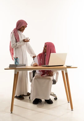 مناقشة الدروس بين الطلاب، تأدية الواجبات المدرسية، العمل الجماعي والتعاون بين الزملاء، بورترية لطالب عربي خليجي سعودي يرتدي الثوب الابيض و المشاغ يجلس على الطاوله امام الحاسب المحمول يقوم بمشاركة المعلومات مع زميلة، فصل دراسي جديد، التعليم في المملكة العربية، خلفية بيضاء
