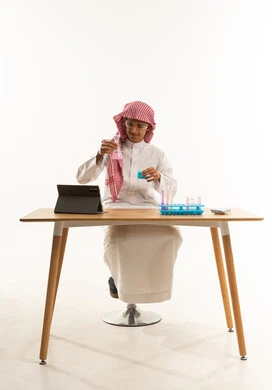 A portrait of a Saudi Gulf Arab student wearing a white thobe and a shemagh, with protective glasses, sitting behind a testing table with sample tubes and chemical analyses, using experimental educational tools and means, effective learning methods utilizing technology and technological devices, with a white background.