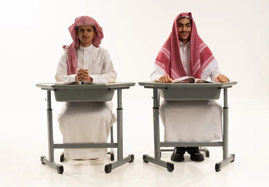 Looking at the camera with gestures of happiness and joy, the back-to-school season, gestures of diligence and excellence, a portrait of two Arab Gulf Saudi students wearing white thobes and shemaghs sitting at a table reviewing lessons for studying and school tests, with a white background. Looking at the camera with gestures of happiness and joy, the back-to-school season, gestures of diligence and excellence, a portrait of two Arab Gulf Saudi students wearing white thobes and shemaghs sitting at a table reviewing lessons for studying and school tests, with a white background.