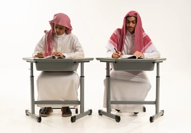التربية والتعليم بالمناهج المقررة للطلاب في المملكة العربية السعودية، إيماءات الاجتهاد والتفوق, بورترية لطالبان عربيان خليجيان سعوديان يرتديان الثوب الابيض و الشماغ يجلسان على الطاولة يقومان بمراجعة الدروس للمذاكرة والاختبارات المدرسية، خلفية بيضاء